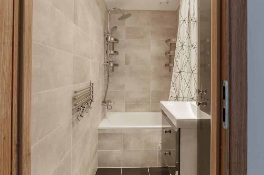 De badkamer is modern en stijlvol afgewerkt met wandtegels in een grijstint en antracietgrijze vloertegels.