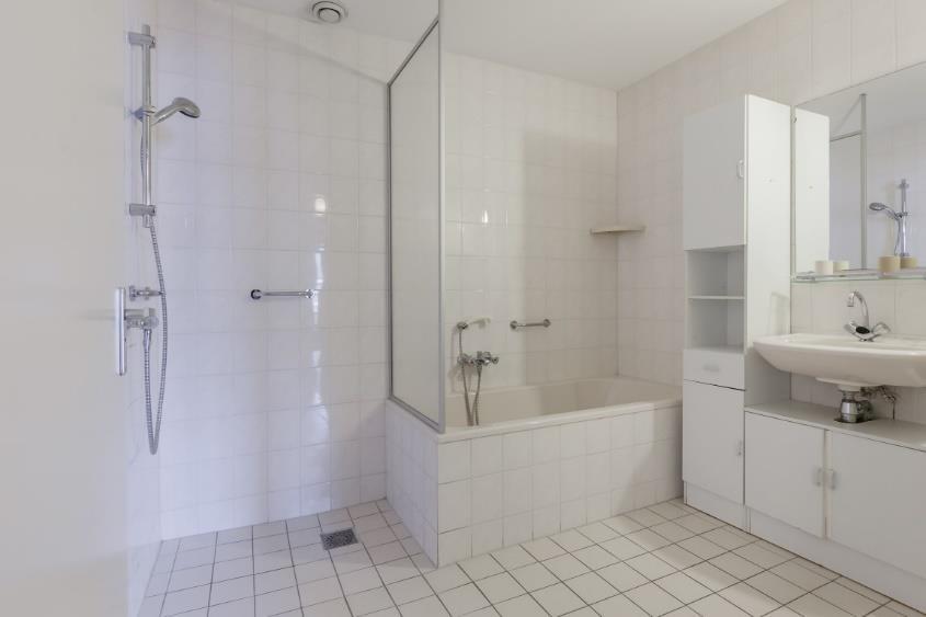 Zowel de badkamer als de separate toiletruimte zijn volledig betegeld met lichte wand-/ en vloertegels.