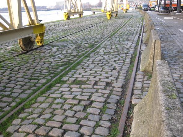 15 16 De wandeling loopt langsheen de kade, evenwijdig met de rails. De strook aan de walzijde van de betonblokken is eveneens verhard in kasseistenen. Hier is de algemene staat iets beter.