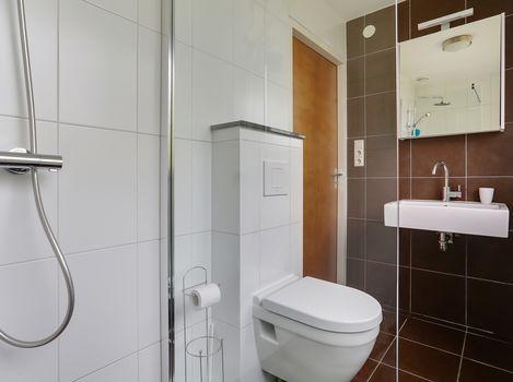 De badkamer is geheel betegeld met een stortdouche voorzien van een vaste wastafel, modern