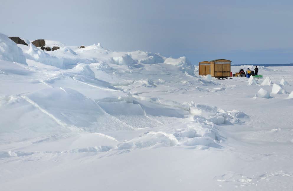 IJskamp Mobiele houten hutjes op ski s houden ons warm vóór en na de duik. Stevig houd ik me vast aan de slee die door een sneeuwscooter wordt voortgetrokken. «Harder! Meer gas!