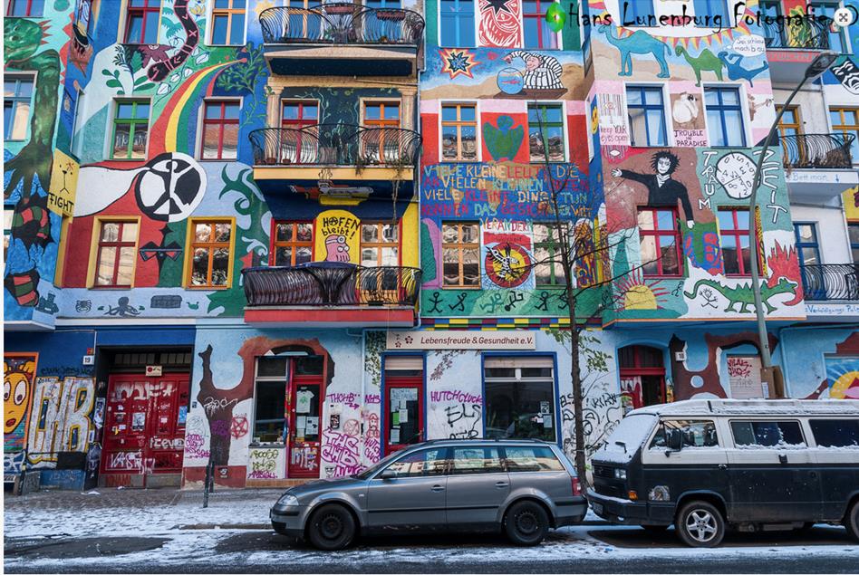 Ik zie op de schilderijen op de huizen een regenboog met een slang erboven, groene blaadjes, draken en onderaan de huizen zie ik slordiger schilderwerk en graffiti tags.