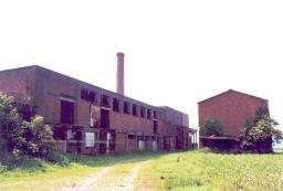 Rijksweg z.nr. (tussen nrs. 93 en 95). Vlasfabriek, bestaande uit 20ste-eeuwse fabrieksgebouwen, schoorsteen en vlasschuren. Roodbakstenen gebouwen.