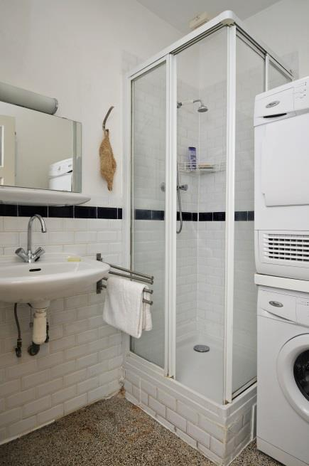 De eenvoudige badkamer is voorzien van een wastafel, een douche en hier is ook de wasmachine- en drogeraansluiting. De badkamer is gedeeltelijk betegeld met een witte tegel en een zwarte rand.