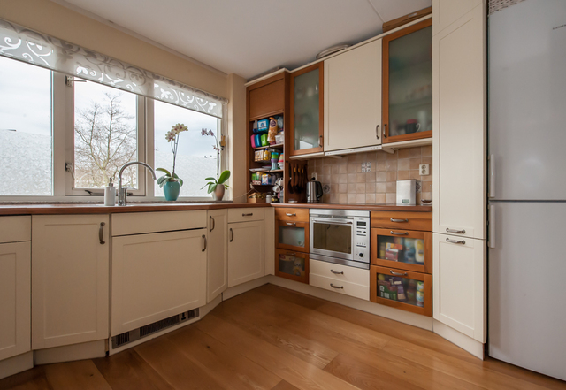 De eetkamer staat in open verbinding met de lager gelegen woonkamer welke is voorzien van hoog plafond en een glaspui met tuindeur.