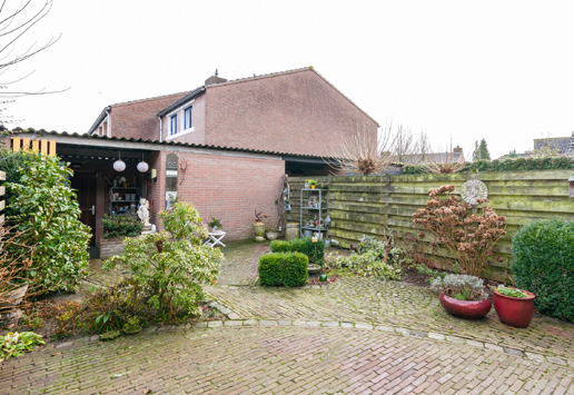 Achter in de tuin staat een stenen berging met overkapping die