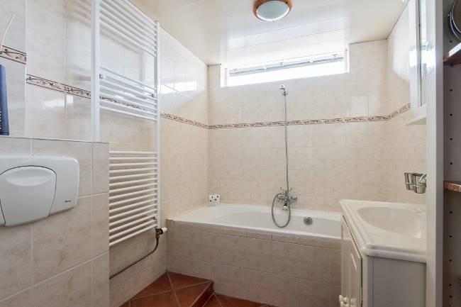 De comfortabele badkamer is geheel betegeld in een lichte tint en heeft contrasterende tegels in een terra kleur op de vloer.
