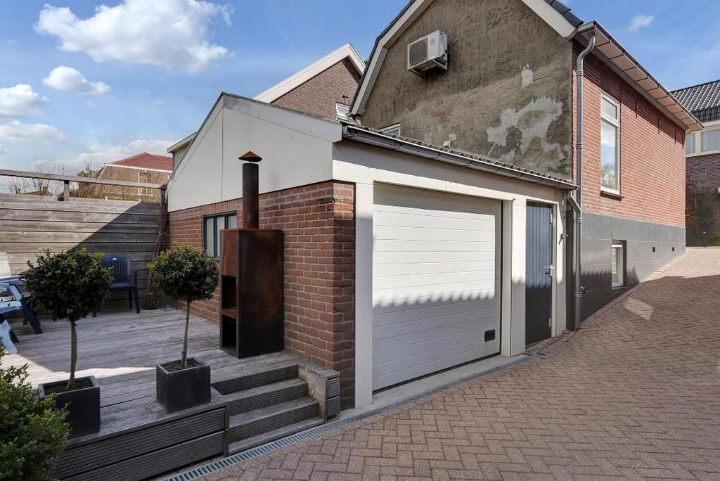 RONDOM DE WONING - Aan de linkerzijde bevindt zich de oprit richting de garage. - Aan de achterzijde is een terras gecreëerd van houten vlonderdelen.