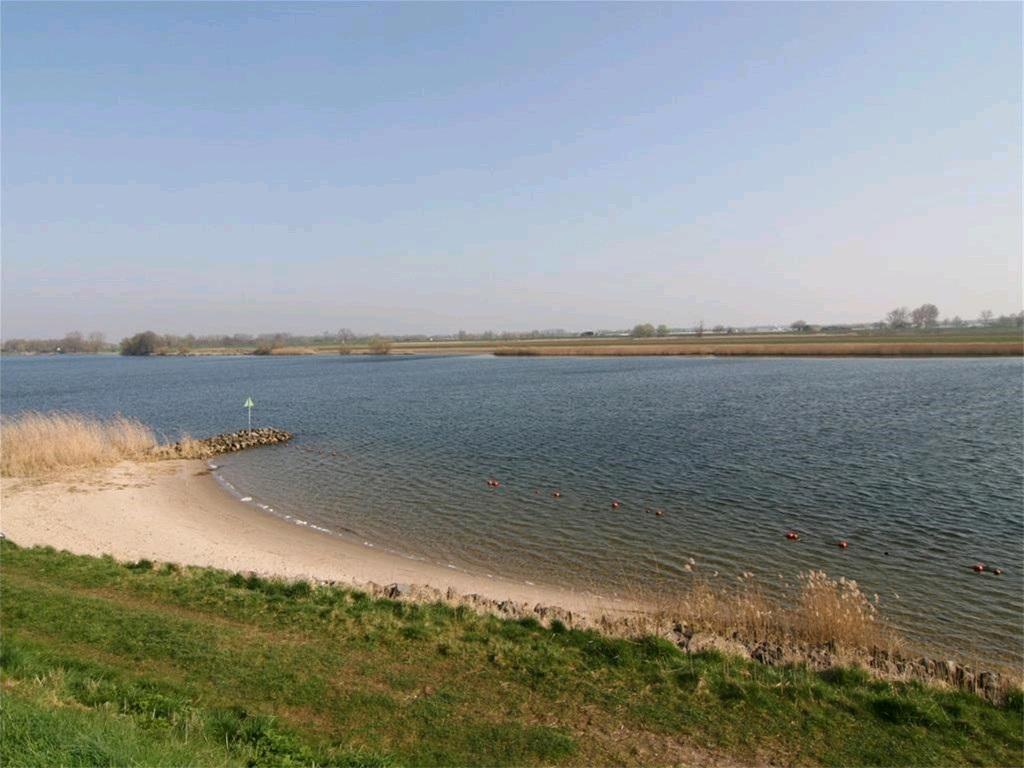 OMSCHRIJVING: Rustig kabbelt het water van rivier de Maas voort. In de verte ziet men de omtrekken van de Wilhelminasluis.