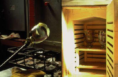 Figuur 1-37: a. De vaas wordt van de blaaspijp afgetikt. Het breekpunt blijft wat ruw. Dit wordt het pontilmerk genoemd. b. Binnen 35 seconden moet de vaas in een afkoeloven van 535 ºC worden gezet.