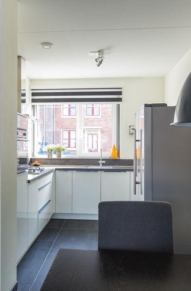 Open keuken met L-vormige in hoogglans wit uitgevoerde moderne keuken voorzien van gaskookplaat, afzuigkap, combi oven,