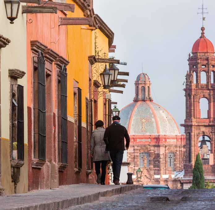 12 Mexico Pedestrians walk toward the dome of Las Monjas Church and spire of the San Francisco Church in the historic center of San Miguel de Allende.
