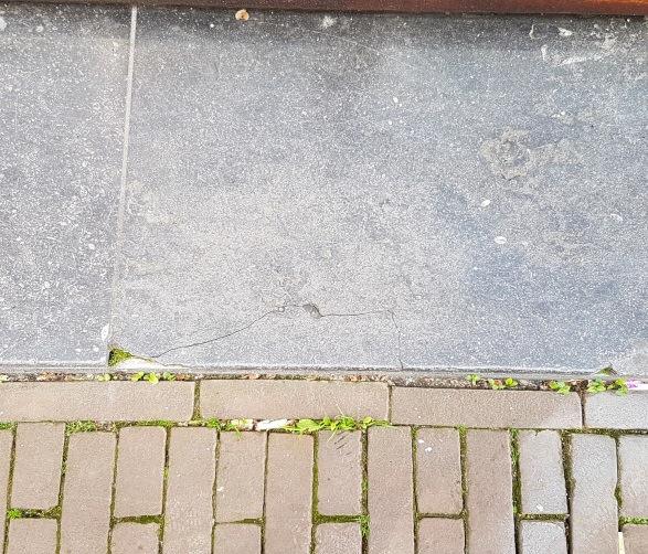 Buitenterrein De natuurstenen platen die bij de commerciële ruimtes liggen bij de overgang van het gebouw naar de openbare weg zijn op veel plaatsen gebroken.