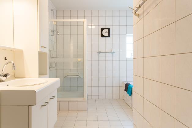 De ruime, geheel betegelde badkamer is uitgevoerd in een lichte kleurstelling