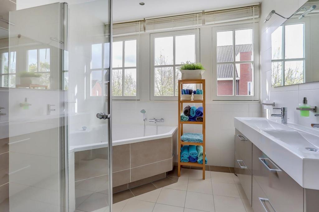 De moderne en geheel betegelde badkamer (ca. 2.76 x 2.57 m) met dakkapel is voorzien van een jacuzzi, een douche, een badmeubel met dubbele wastafel, vloerverwarming en een designradiator.