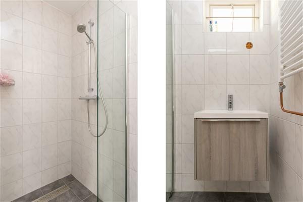 De geheel betegelde doucheruimte is ingericht met een inloopdouche, een wastafel met bergmeubel, inloopdouche en design radiator.