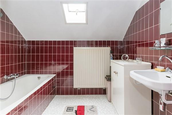 De bijna geheel betegelde badkamer is uitgerust met een bad-/douchecombinatie, een wastafel en een klein dakvenster.