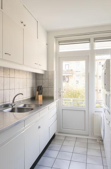 Dichte keuken met witte opstelling voorzien van vloertegels, rvs aanrechtblad, veel kastruimte,