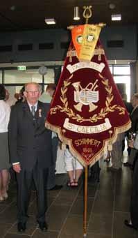 Ge Soons was een van de mensen in het complot en heeft Jean verteld dat in het gemeentehuis iets met de voorzitter van de fanfare op stapel stond en dat hij met het onze drapeau erbij moest zijn.