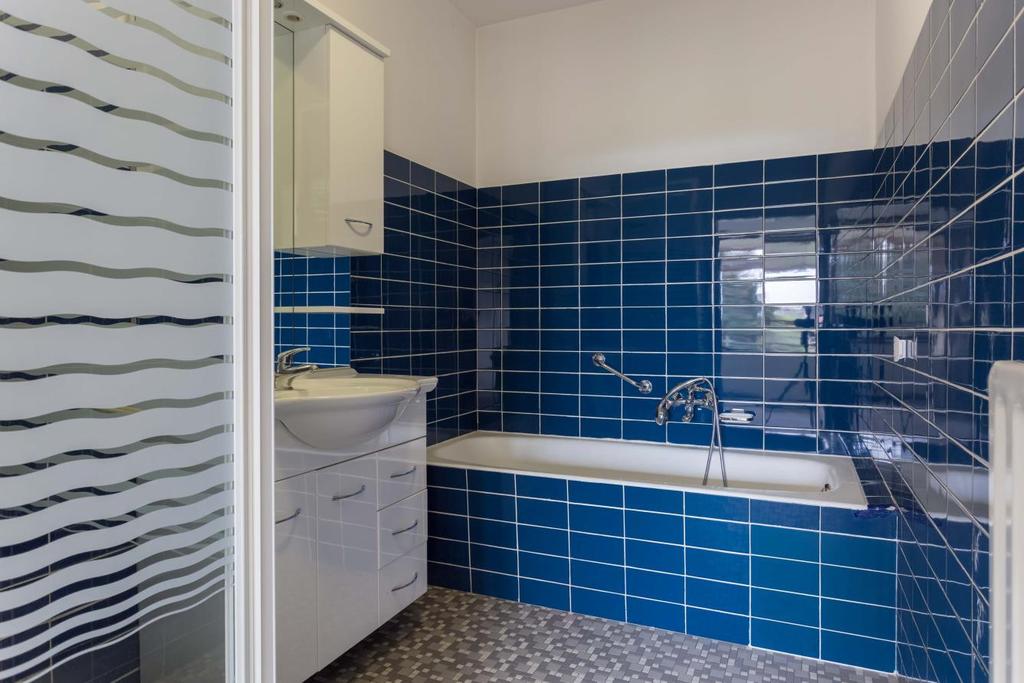 De ruime badkamer is gedeeltelijk betegeld en uitgevoerd met een ligbad met thermostatische kraan,