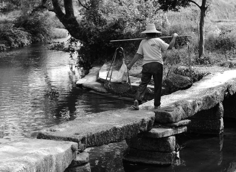 Over een oude stenen brug vervoeren de dorpsbewoners hun goederen in rieten manden, alsof de tijd heeft stilgestaan T e midden van een landschap dat bestaat uit levendige dorpjes, boerderijen,