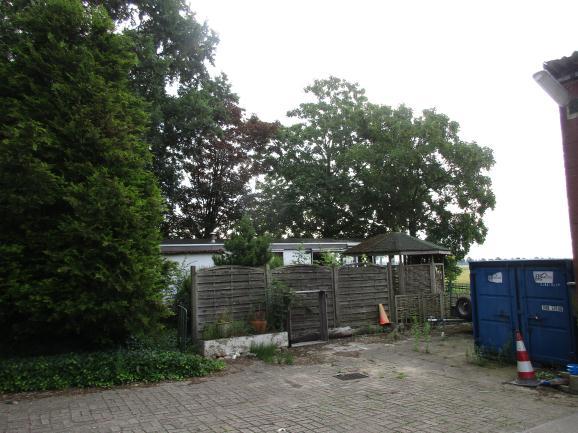 In het plangebied bevinden zich twee schuren, een loods, vier zeecontainers, een stacaravan, bomen en struikgewas.