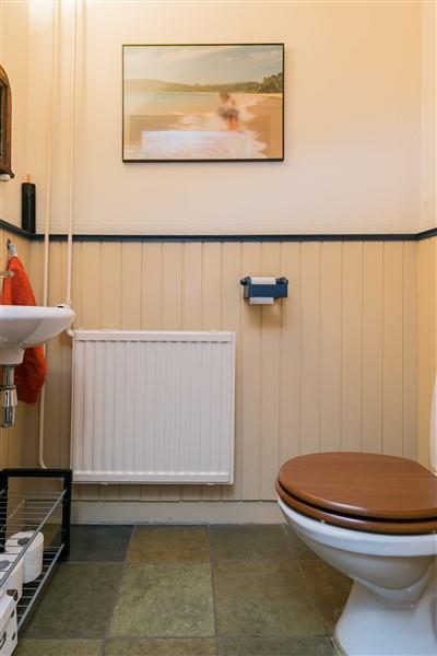De toiletruimte is voorzien van een plavuizen vloer, houtenlambrisering en een