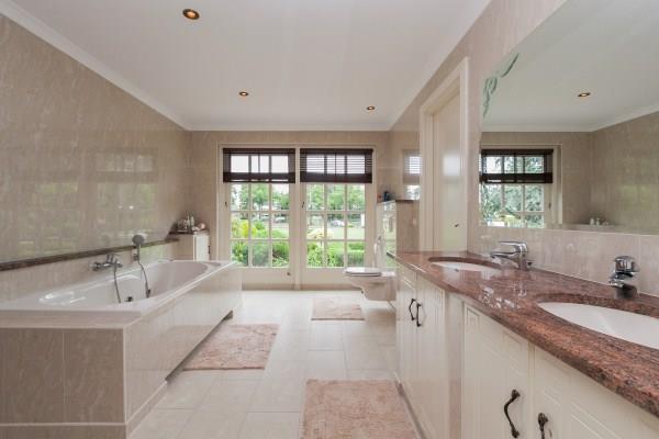 De geheel met gepolijste tegels betegelde badkamer is uitgerust met een ligbad (bubbelbad), een separate douche met glazen