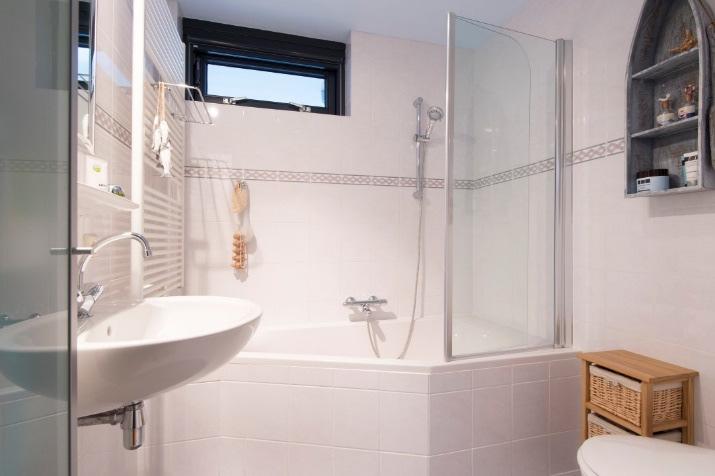 De comfortabele badkamer is geheel betegeld in een lichte kleurstelling. De sanitaire uitrusting bestaat uit een ligbad met thermostaatkraan en douchegarnituur.