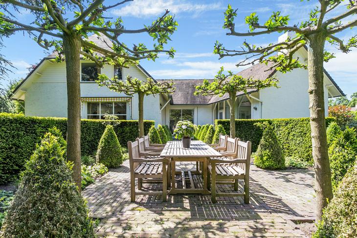 EXTERIEUR De woning bestaat uit twee tuinen: een kleinere patiotuin met buxusvakken aan de achterzijde van de woning en een hoofdtuin aan de voor en zijkant van de woning.