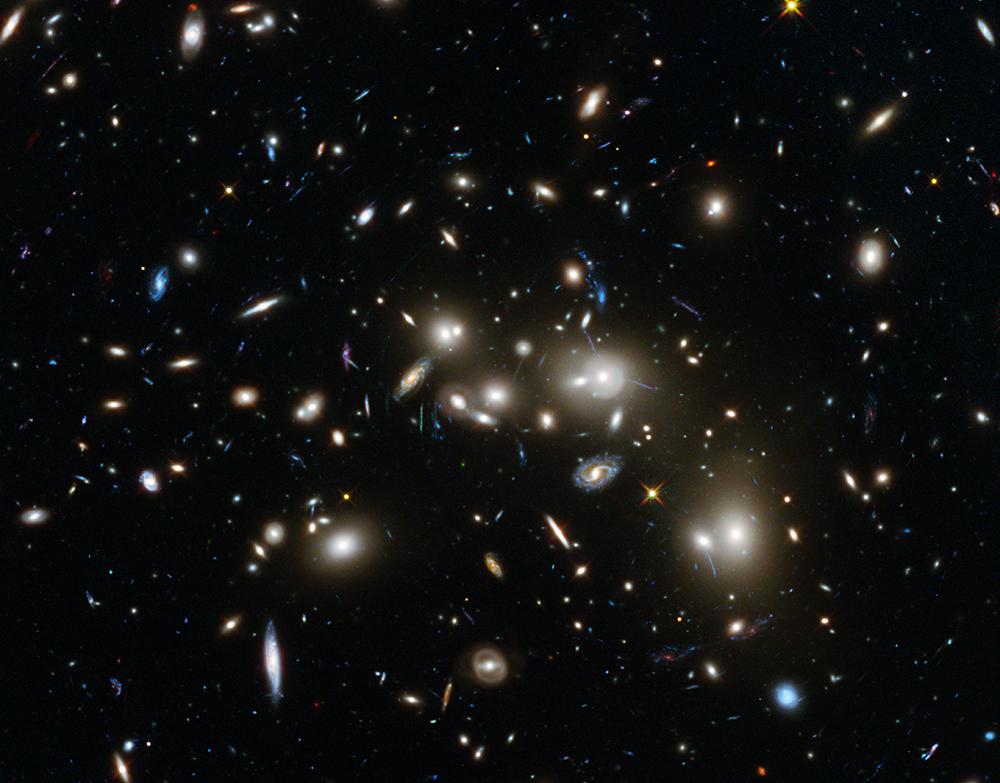 Figuur 8.2: Links: Voorbeeld van een cluster van sterrenstelsels, Abell 2744. Veel van de sterrenstelsels in dit plaatje (niet die op de achtergrond) bewonen dezelfde halo, en draaien om elkaar heen.