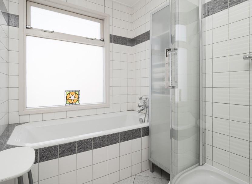 Nette geheel betegelde lichte badkamer met een vaste wastafel, douche,