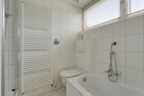 De badkamer is geheel wit betegeld en beschikt over een dakkapel met kunststof kozijnen, een