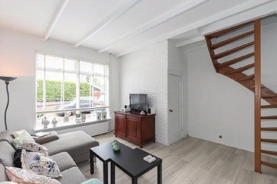 30, gezellige woonkamer met balkenplafond, spachtelputz wanden, laminaatvloer, open houten trap naar de verdieping en een eethoek naast de open keuken.