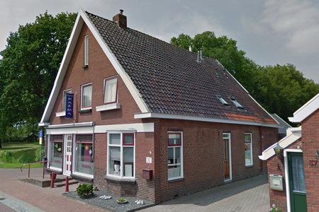 Symmetrisch opgezet woonhuis onder schilddak uitgevoerd met decoratieve elementen in eclectische stijl. Beeldbepalende ligging in het lint aan de Huningaweg.