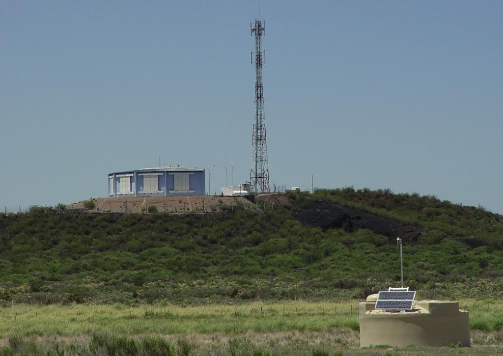 Deeltjesdetector met op de achtergrond een gebouw met fluorescentietelescopen, onderdeel van het Pierre Auger Observatorium. Foto: Pierre Auger Observatorium.