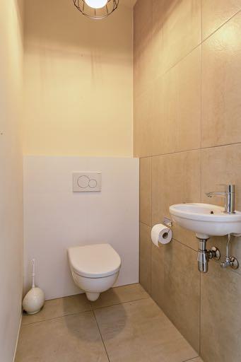 Het aparte ruime toilet is geheel betegeld en is voorzien van een hangend toilet en een fontein.