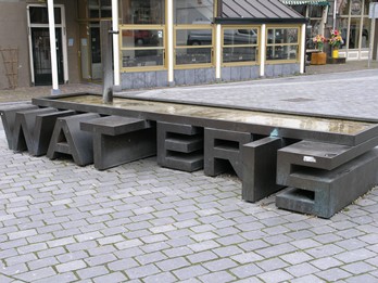 kunstenaar: Marc Ruygrok titel: WAT-ER-IS jaartal: 2000 locatie: Ganzenheuvel/Hezelstraat Dit kunstwerk bestaat uit een watertafel, waarvan de poten zijn gevormd uit de letters WAT ER IS.
