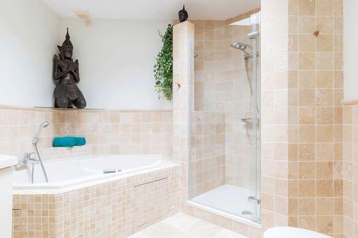 Deze badkamer is voorzien van een badmeubel met een wastafel en een mengkraan, een groot ligbad met whirlpool, een douche met