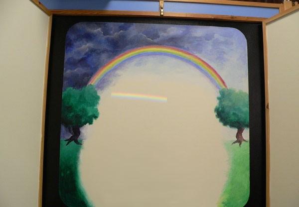 Kijk naar het witte projectievlak: er staat nu een regenboogje! Kijk met de kinderen naar de regenboog. Het witte licht uit de projector is niet echt wit, alle kleuren van de regenboog zitten er in!