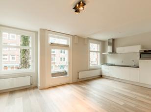 De woonkamer met open keuken is voorzien van openslaande deuren naar het balkon, twee inbouwkasten waarvan één is voorzien van de