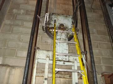SITUATIE 5 Tijdens een herbekabeling werkt de monteur met behulp van een ladder aan de schijf bovenaan het tegengewicht op 5 m boven de vloer.