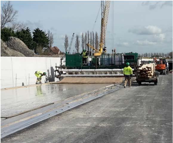 Achter de tweede glijbekistingsmachine bevindt zich een supersmoother. Deze zal kleine oneffenheden die ontstaan zijn tijdens het verdichten van het beton wegwerken.