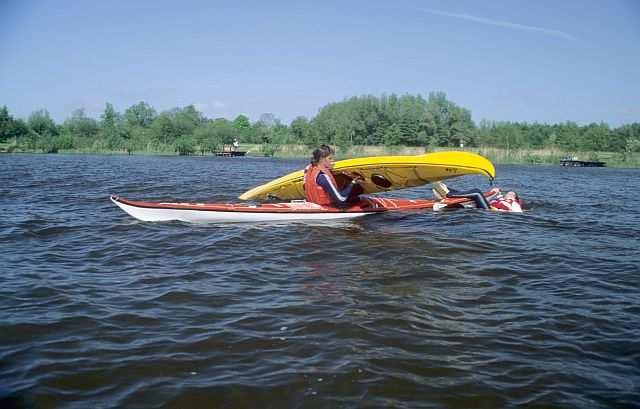 De redder tilt de voorpunt van de omgeslagen kano uit het water en trekt de boot in omgekeerde positie over zijn kano heen, tot de kuipopening over zij spadzijl ligt.