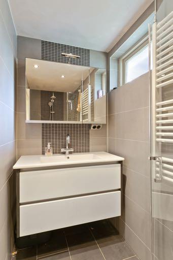 De gemoderniseerde geheel betegelde badkamer is voorzien van een inloopdouche met regendouche en handdouche en een thermostaatkraan, een badmeubel met
