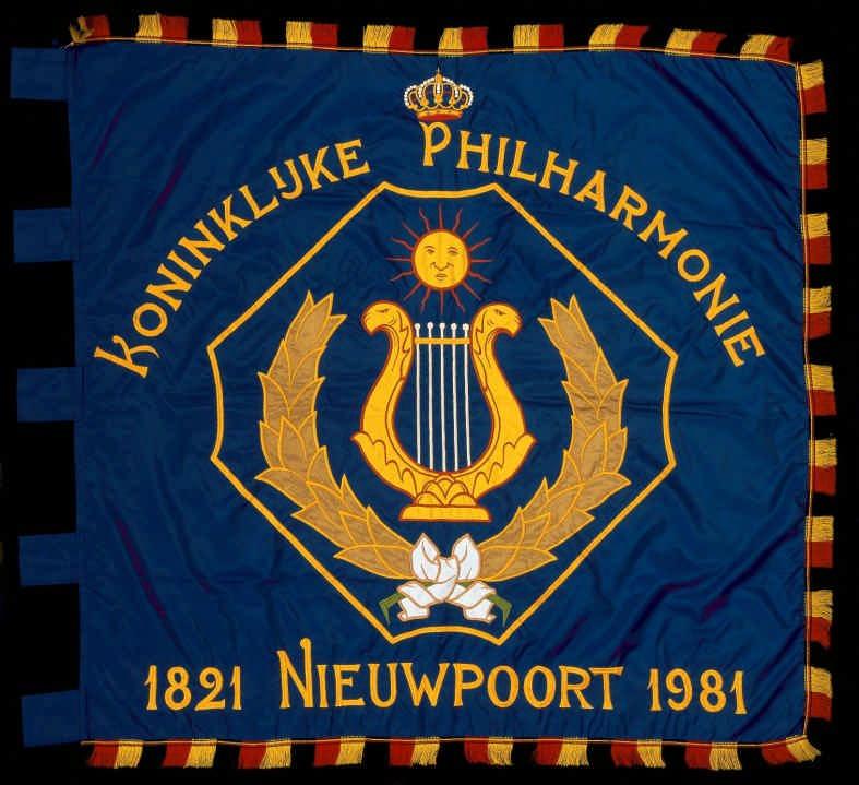 Nr. 67 Nieuwpoort 1981 Koninklijke Philharmonie nylon borduurwerk, incrustatie meerkleurig, zwart/geel/rode franjes 110 x 115 cm lussen aan de broekzijde 8 x 9 cm Centraal in blauw veld een