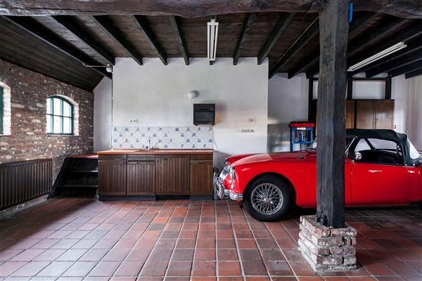 De garage/werkplaats werd bij gebruik als gastenverblijf ingericht als woonkamer en is thans voorzien van een plavuizen vloer en een houten balken plafond.