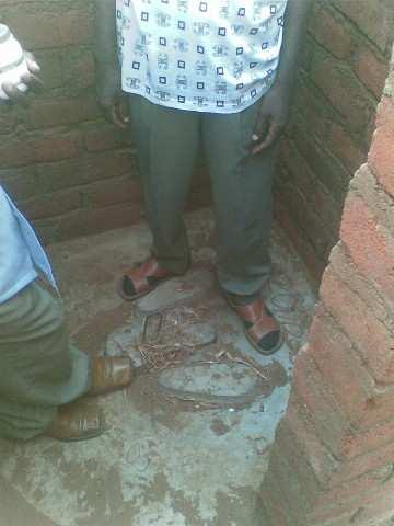 Rechts een faciliteit om handen te wassen. Foto 2 Een van de HSAs poseert bij een pit latrine en een faciliteit om handen te wassen.