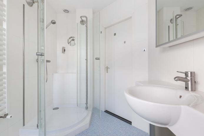 De badkamer is voorzien van een duo ligbad, douchecabine met thermostaatkraan, wit badkamermeubel en