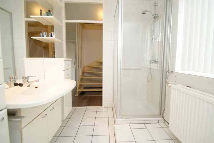 Foto boven: De badkamer is betegeld met witte tegels en voorzien van een